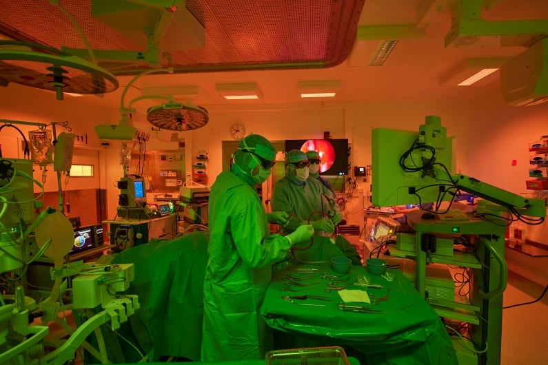 Surgeon performing a procedure in an operating theatre with ergonomic lighting in greenish and reddish hues