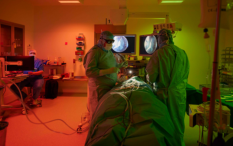 Operationsstue oplyst i grønlige og rødlige lyszoner med kirurg der udfører procedure