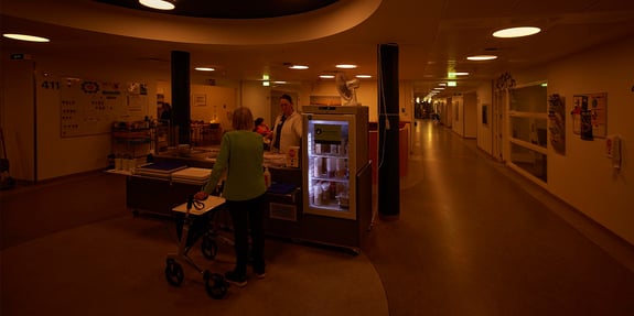 Sygeplejerske snakker med patient ved kantine på hospitalsafdeling med døgnrytmelys