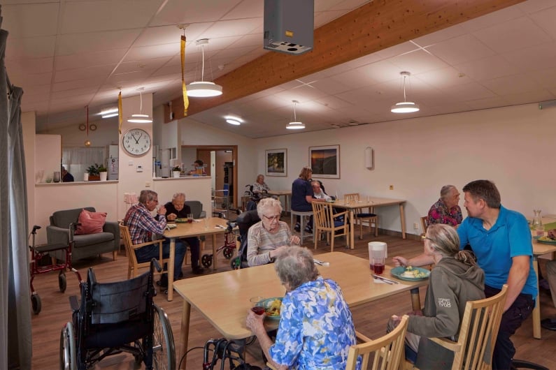 Nursing home residents eat lunch in a community room while the staff assists them