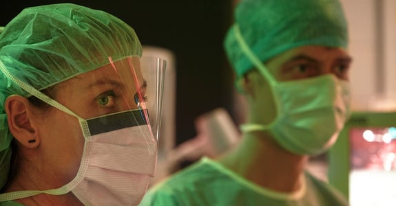 Surgeons look at a screen during surgery while Chromaviso's ergonomic light can be seen in red and green color tones in the background