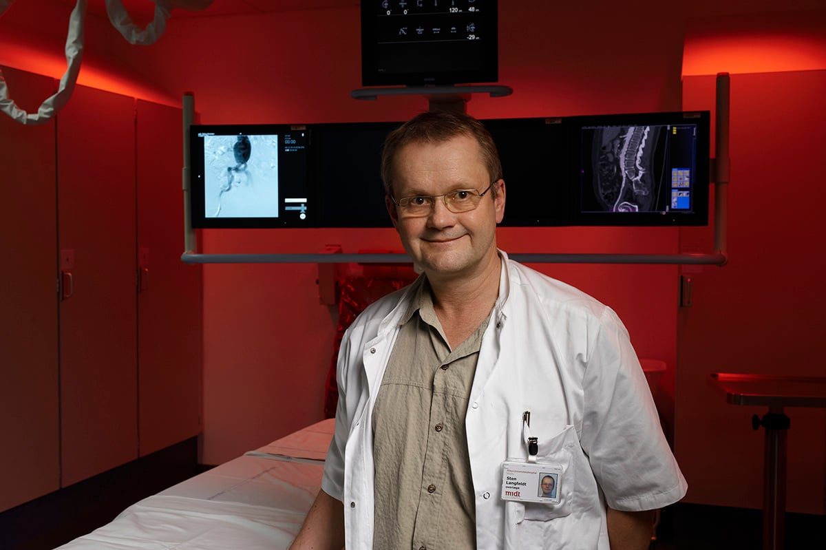 Överläkare Steen Langfeldt står i sjukhusrummet med ergonomiskt ljus och röntgenbilder i bakgrunden